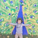 Kid posing in front of a peacock wall art piece